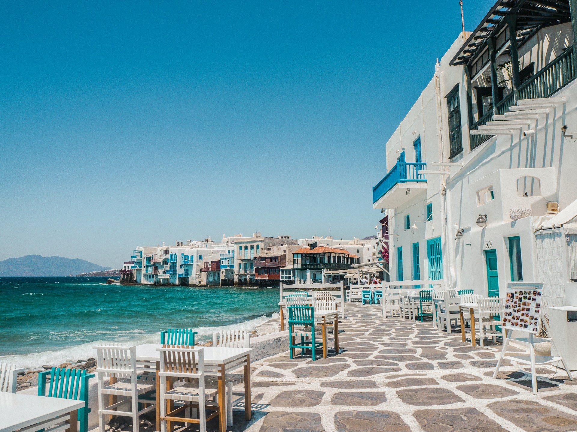 Chairs and tables outside a restaurant in a Greek harbor