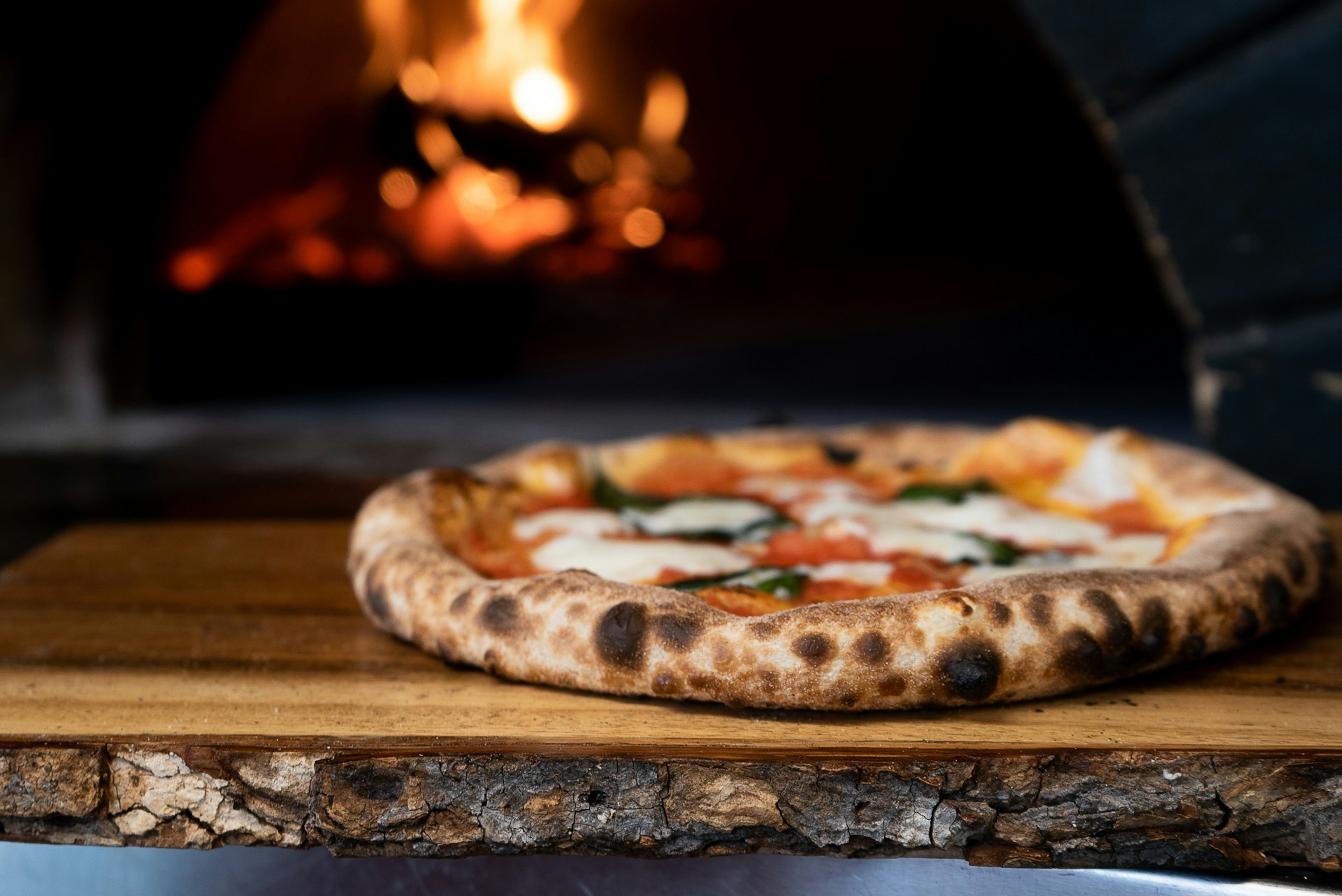 A freshly cooked pizza with a pizza oven in the background