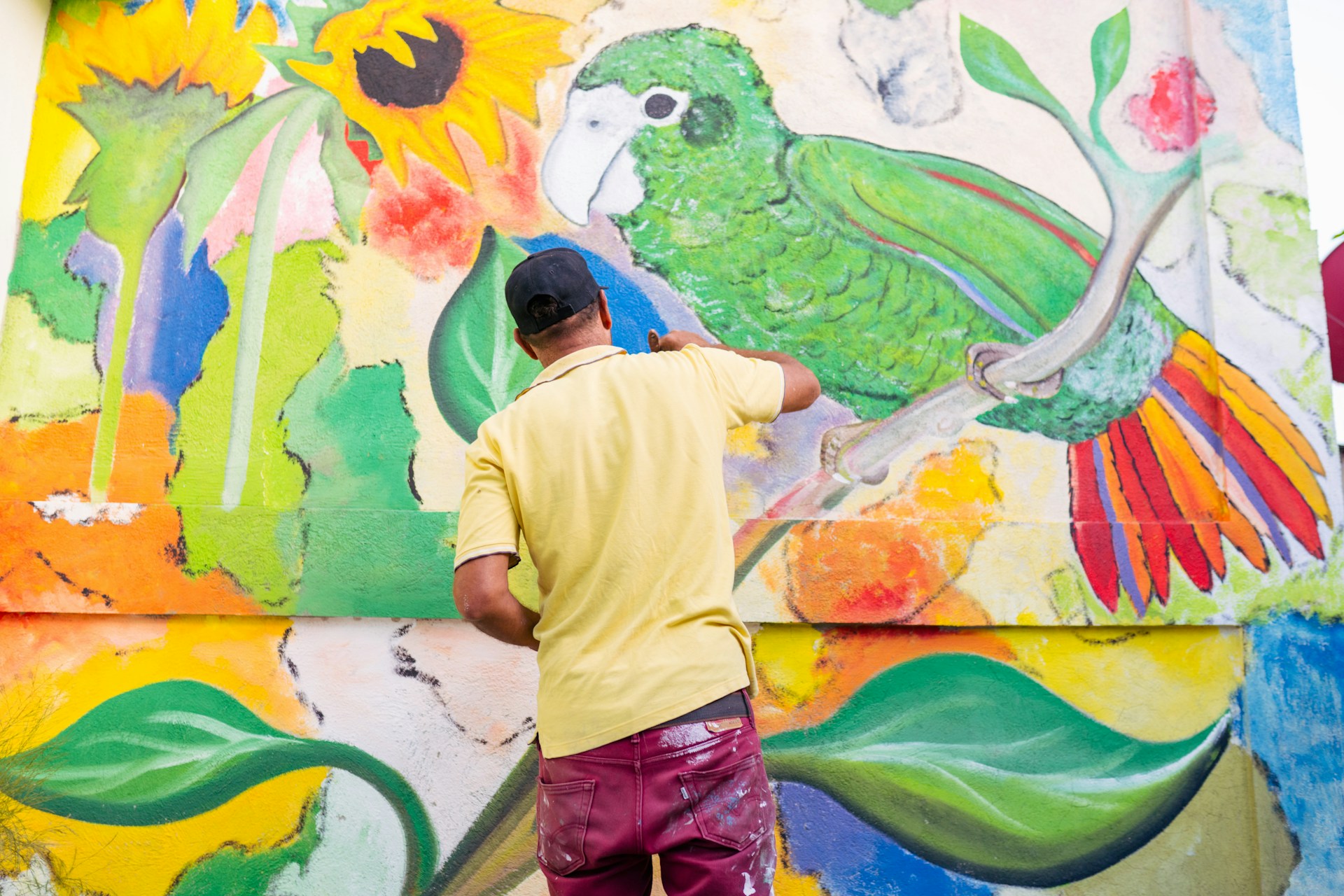 a man painting a mural of flowers and parrots