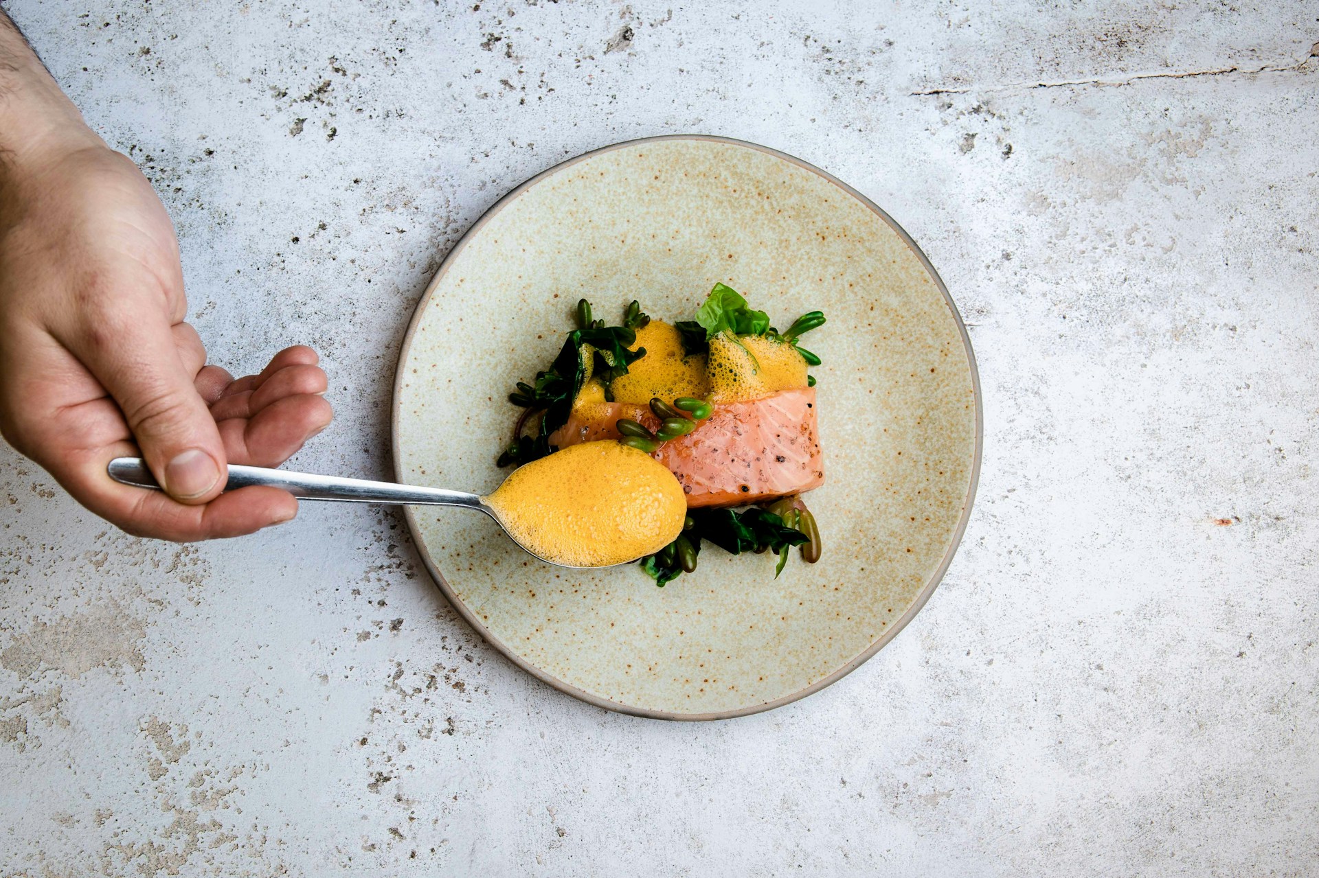 A chef adding dressing to a plate of salmon