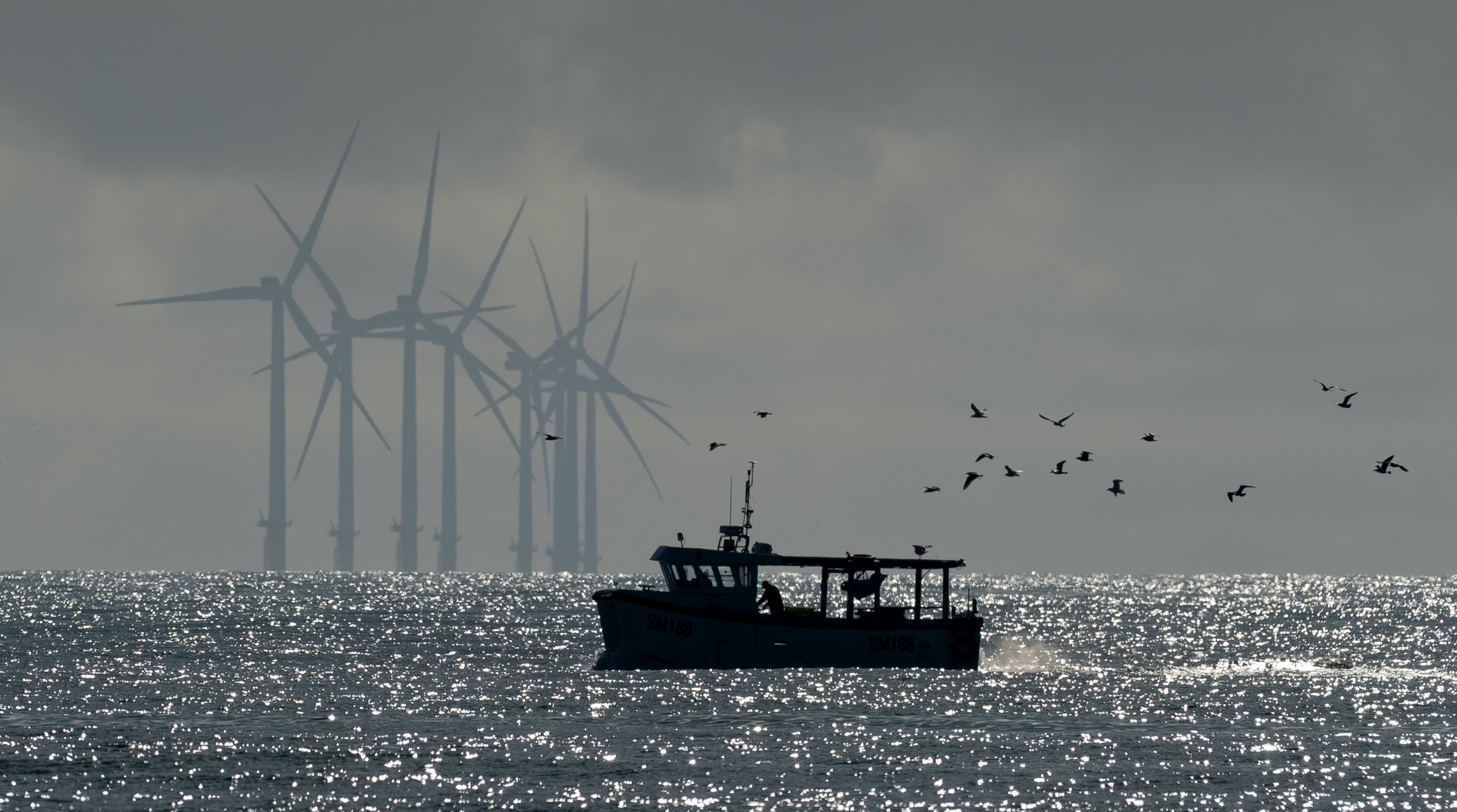 Silhouette of a fishing trawler with wind turbines in the background