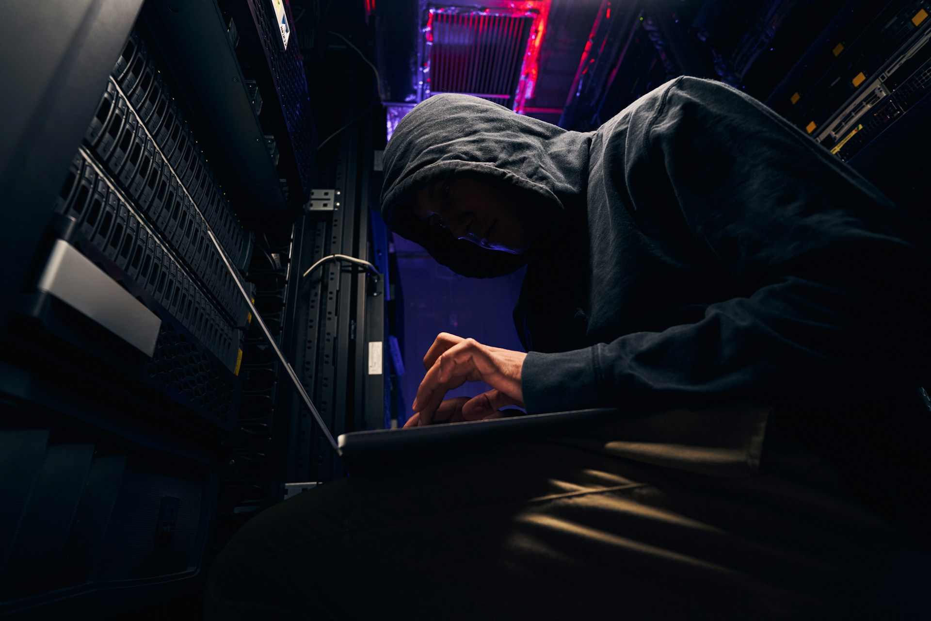 A hooded computer hacker bent over a laptop