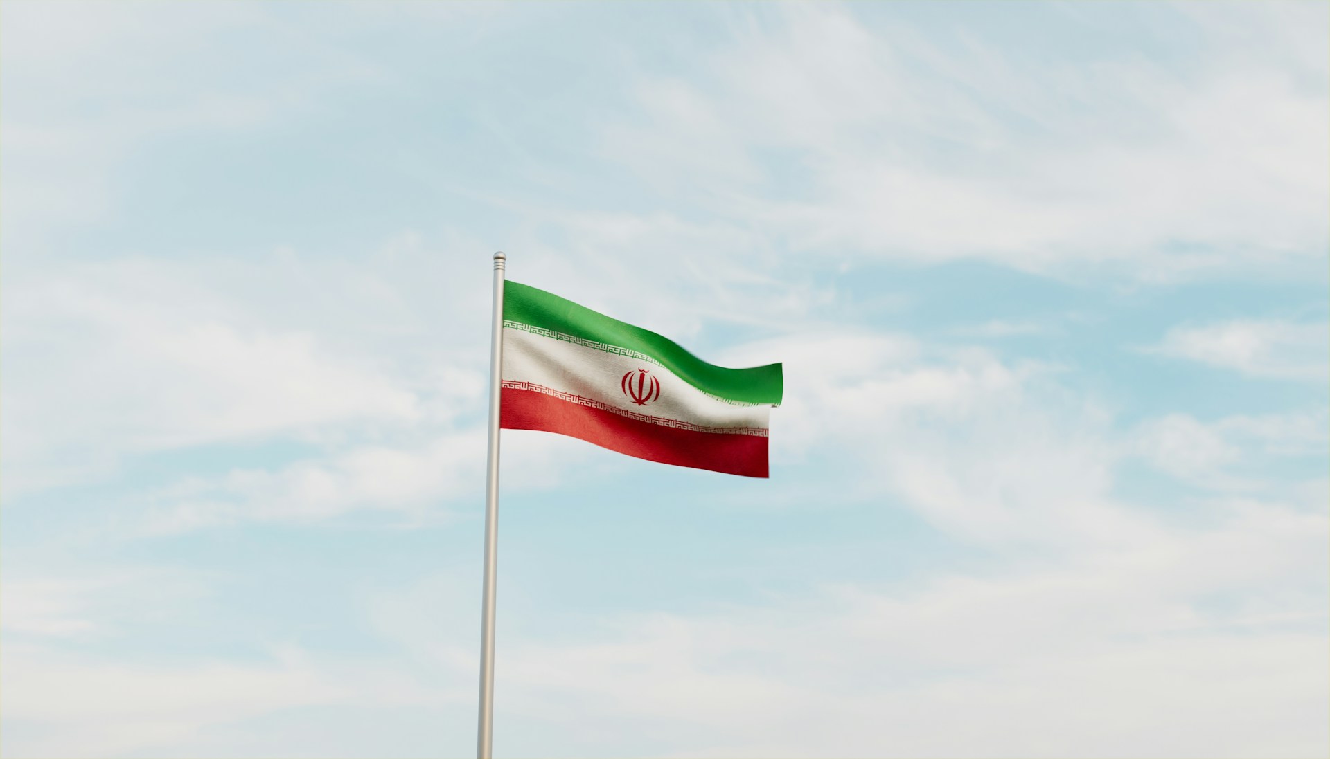 The Iranian flag flying against a blue cloudy sky